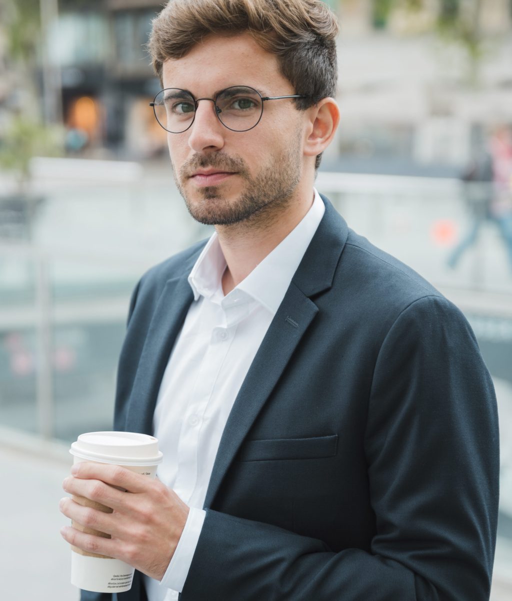 close-up-young-businessman-holding-disposable-coffee-cup-hand-looking-camera